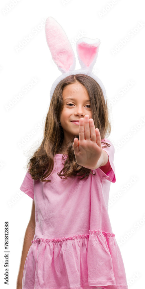 Brunette hispanic girl wearing easter rabbit ears with open hand doing stop sign with serious and confident expression, defense gesture Brunette hispanic girl wearing easter rabbit ears with open hand doing stop sign with serious and confident expression, defense gesture