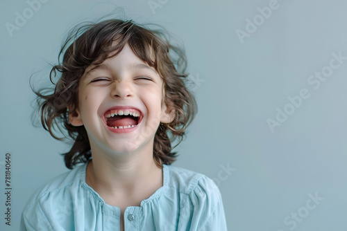 child 10 years, enthusiastic laughing, eyes ope, light blue blouse, light grey background, world laugh day photo