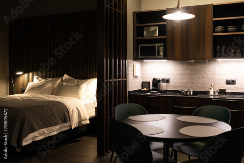 A warm and inviting studio apartment featuring a comfortable bed, well equipped, kitchen and a sleek dining area with subdued lighting
