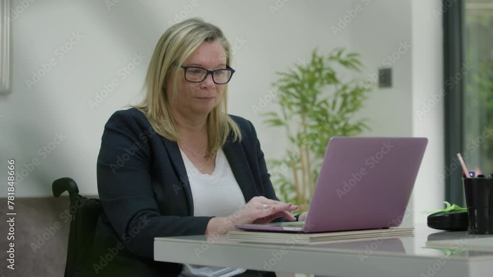 Woman in wheelchair working in home office, peering behind plant Woman in wheelchair working in home office, peering behind plant