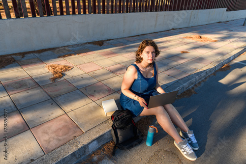 Student girl is sitting on the sidewalk with laptop