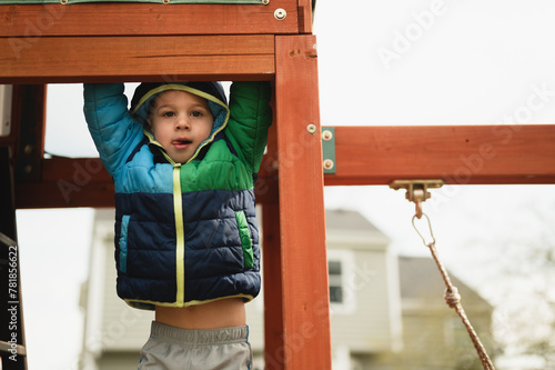 Φωτογραφία Happy child boy swinging on playset in coat in the winter outdoors