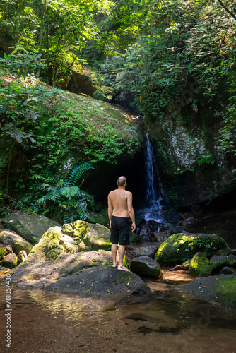 Adult man bathing on cave entrance waterfall in green atlantic forest