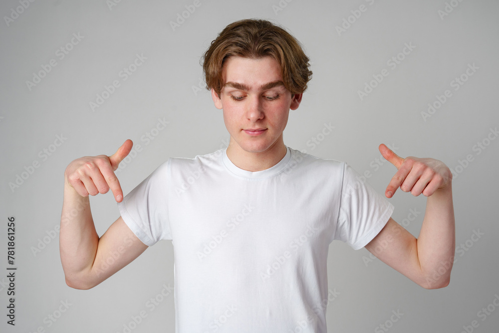 Young Man in White T-Shirt Pointing Downwards With Both Hands Against Plain Background Young Man in White T-Shirt Pointing Downwards With Both Hands Against Plain Background