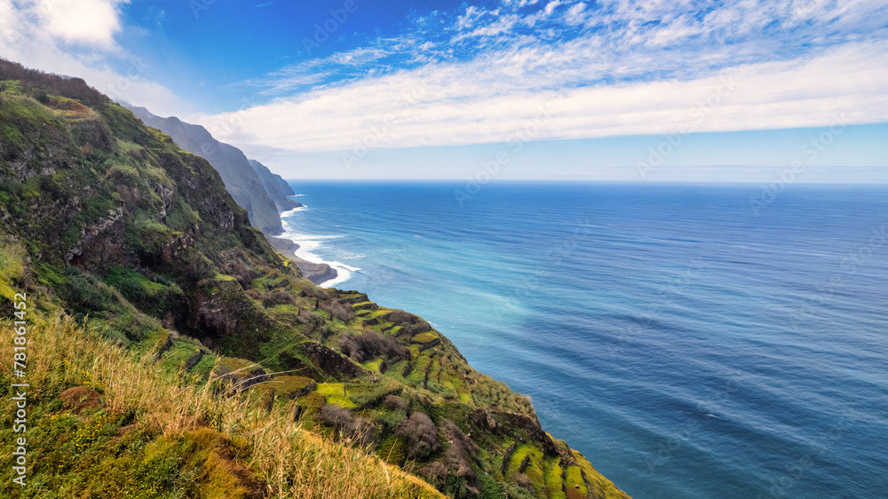 Steep, green slopes of Madeira, covered with vegetation, descending to the blue ocean; fog envelops the mountains, adding mystery to the scenery.