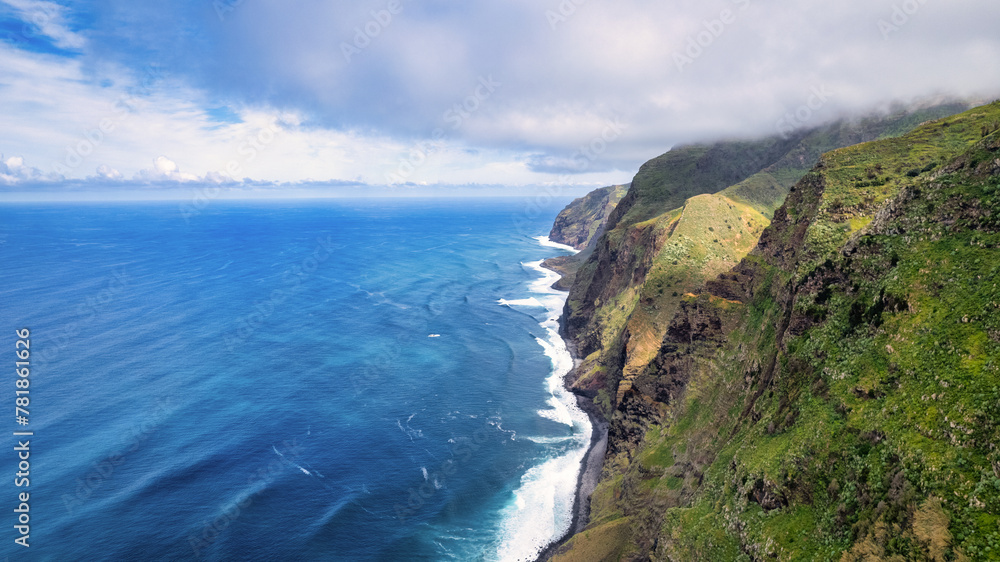 Steep, green slopes of Madeira, covered with vegetation, descending to the blue ocean; fog envelops the mountains, adding mystery to the scenery.