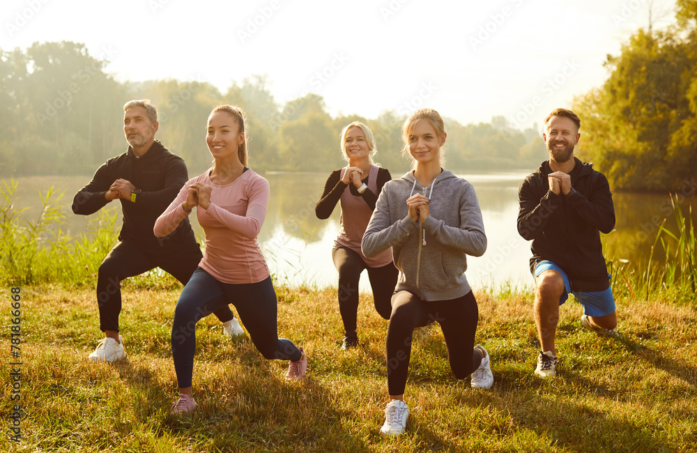 Active sporty people doing stretching exercising in nature. Happy smiling men and women in sportswear having sport workout in the park in the morning. Outdoors training and fitness concept. - obrazy, fototapety, plakaty 