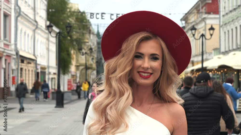 stunning blonde woman in a beautiful white dress is seen walking down a city street. She's making a strong fashion statement with a bold red hat and matching red heels. she turns around. stunning blonde woman in a beautiful white dress is seen walking down a city street. She's making a strong fashion statement with a bold red hat and matching red heels. she turns around.