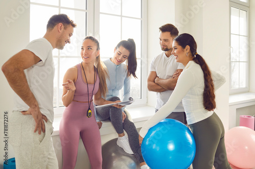 Health centre and fitness club sporty people talking with slim female coach. Discuss how to improve results, overall health and wellness by participating in fitness games, strength training, exercises photo