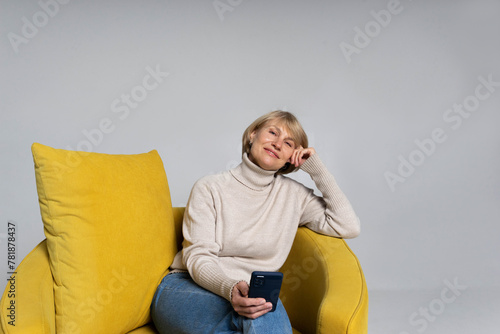 An adult woman sitting on the yellow chair with a phone smiling and doing her routine 