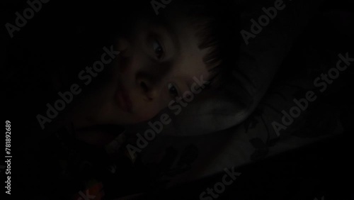 Caucasian boy 10 years old uses a tablet computer or smartphone in the dark while lying in bed. student's addiction to gadgets photo