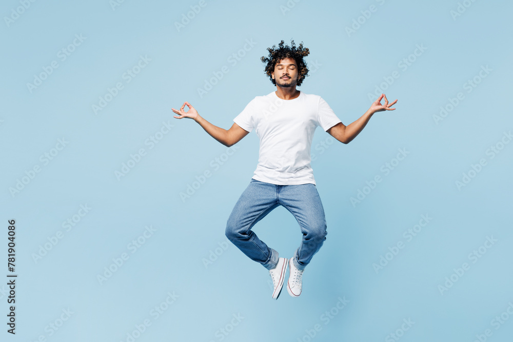 Full body young happy Indian man wear white t-shirt casual clothes jump high hold spreading hands in yoga om aum gesture relax meditate try to calm down isolated on plain light blue cyan background.