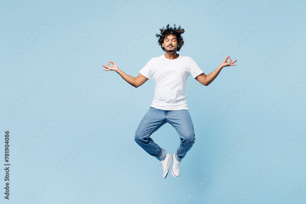 Full body young happy Indian man wear white t-shirt casual clothes jump high hold spreading hands in yoga om aum gesture relax meditate try to calm down isolated on plain light blue cyan background. Full body young happy Indian man wear white t-shirt casual clothes jump high hold spreading hands in yoga om aum gesture relax meditate try to calm down isolated on plain light blue cyan background.