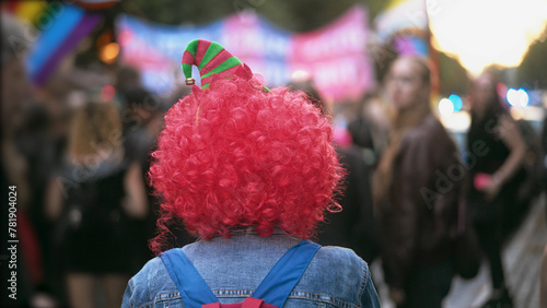 Person wear pink clown wig. Dressed up man enjoy joy festival. Fancy carnival hat. Happy jester have fun child party. Red colorful curly hair. Cute buffoon costume. Comic fest outdoor. Festive show. photo