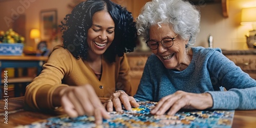 Joyful female aide helping elderly lady with jigsaw at residence.