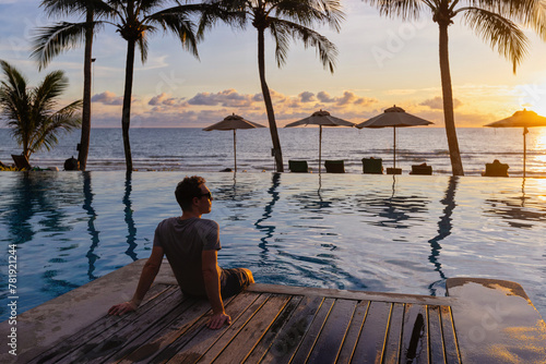 man relaxing near swimming pool in luxurious hotel resort at sunset, beach vacation travel