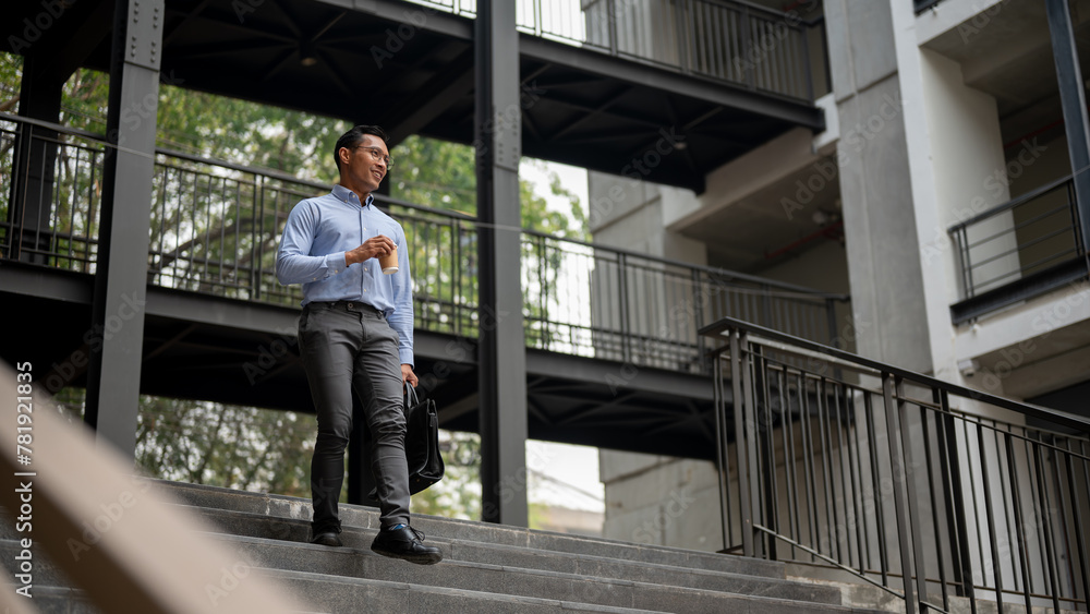 A confident Asian businessman walking down the stairs, holding a coffee cup and a briefcase. A confident Asian businessman walking down the stairs, holding a coffee cup and a briefcase.
