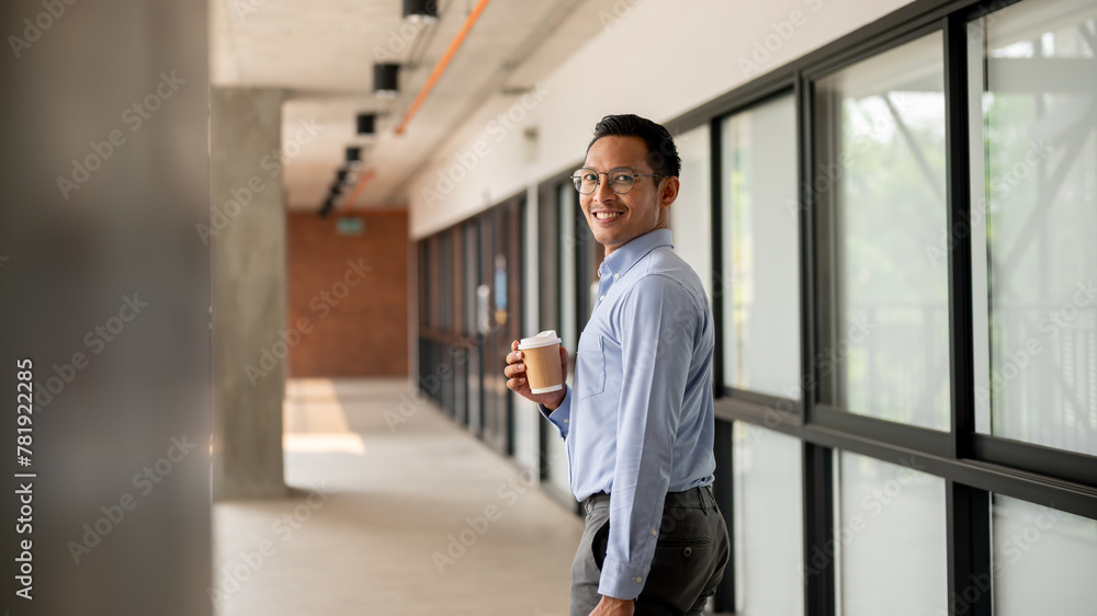 A confident Asian businessman walking along an indoor corridor, holding a coffee cup and a briefcase A confident Asian businessman walking along an indoor corridor, holding a coffee cup and a briefcase