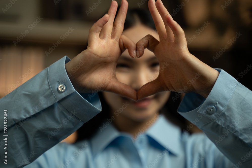 Obraz premium A woman of Asian descent demonstrates how to create a heart shape using her hands. She carefully positions her fingers in a heart formation, showcasing the gesture.