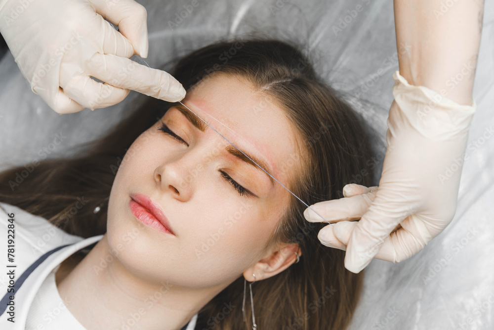 Naklejka premium A cosmetologist applies permanent makeup to the eyebrows - eyebrow tattoo. eyebrow perm