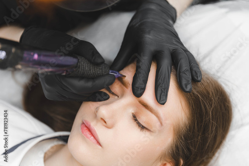 A cosmetologist applies permanent makeup to the eyebrows - eyebrow tattoo. eyebrow perm photo