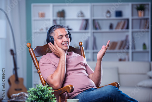 Weekend. Relaxed Indian Man In Wireless Headset Using Mobile Phone Listening To Audiobook Sitting On rocking Chair. photo