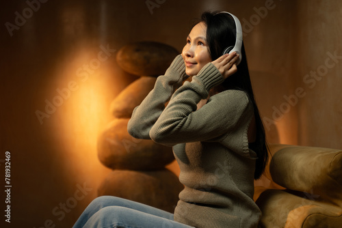 A peaceful woman is immersed in the experience of listening to music using her headphones. Seated comfortably in a warmly lit living area, she appears content and relaxed, with a serene expression