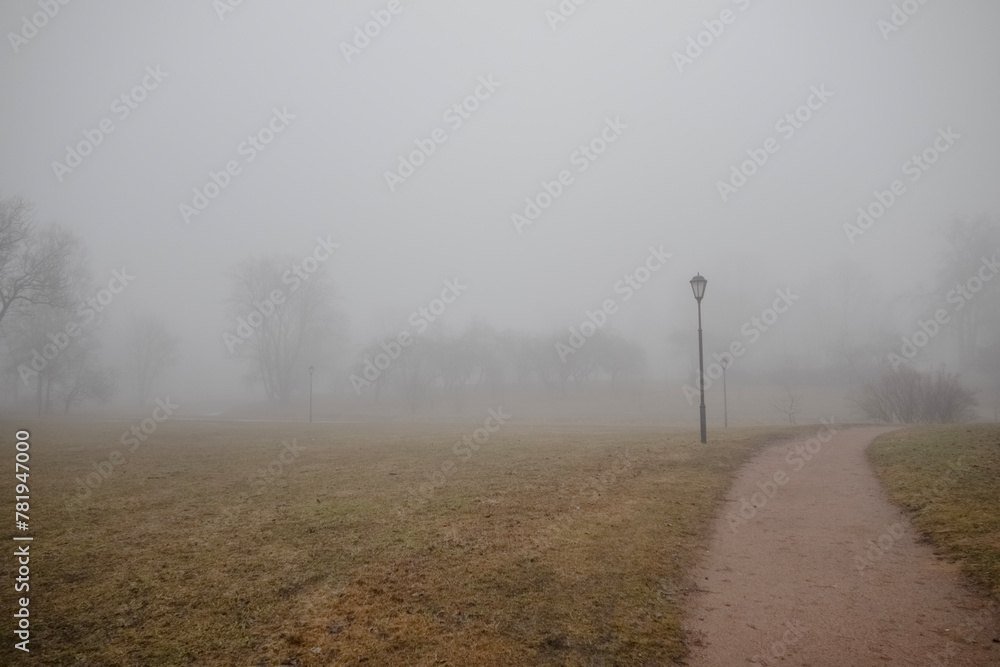 Deserted city park with trees, lanterns and a sandy path in a shroud of morning fog Deserted city park with trees, lanterns and a sandy path in a shroud of morning fog