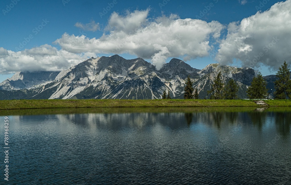 Scenic shot of a mountain range partially covered in snow in front of a still lake Scenic shot of a mountain range partially covered in snow in front of a still lake