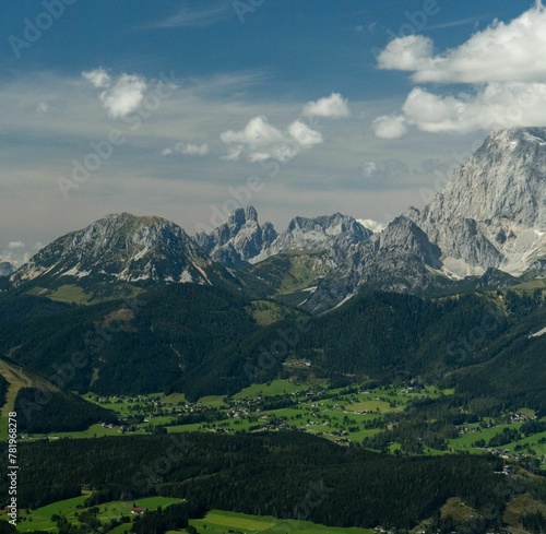 Aerial shot of a locality surrounded by trees and high rocky peaks covered in snow