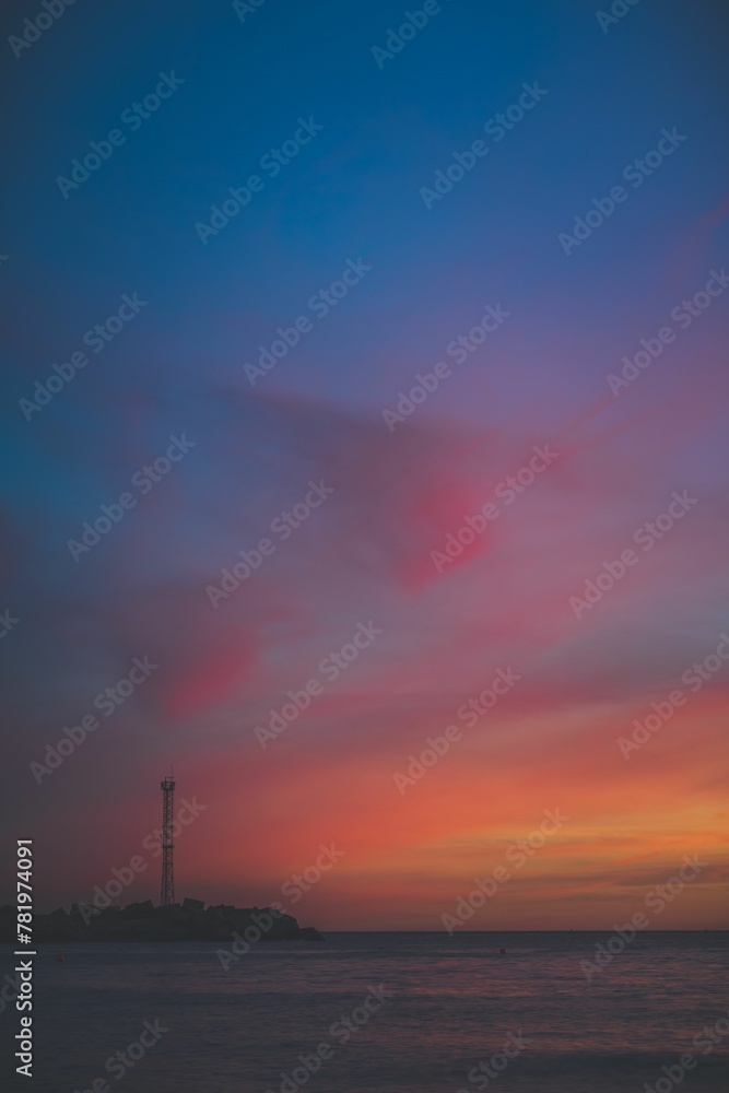 Vertical shot of a beautiful sunset over a tranquil sea against a lighthouse on the beach