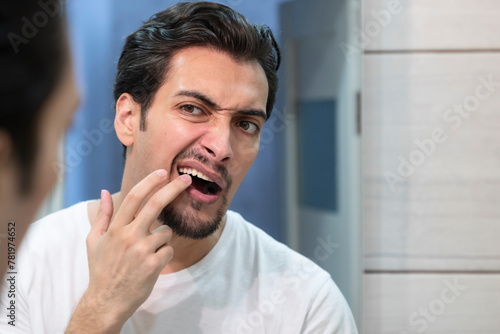 Young handsome man checking up his teeth in front of the mirror in the bathroom