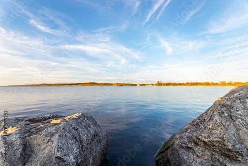 Scenic view of a rocky shore against a tranquil lake under a blue sky on a sunny day