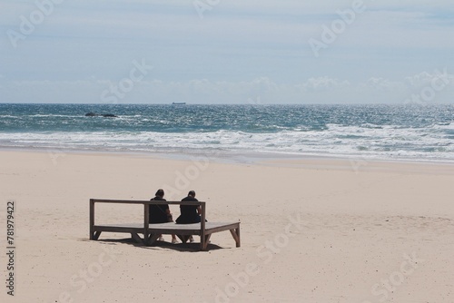 Couple resting on the sandy beach with the foamy sea waves in the background on a sunny day