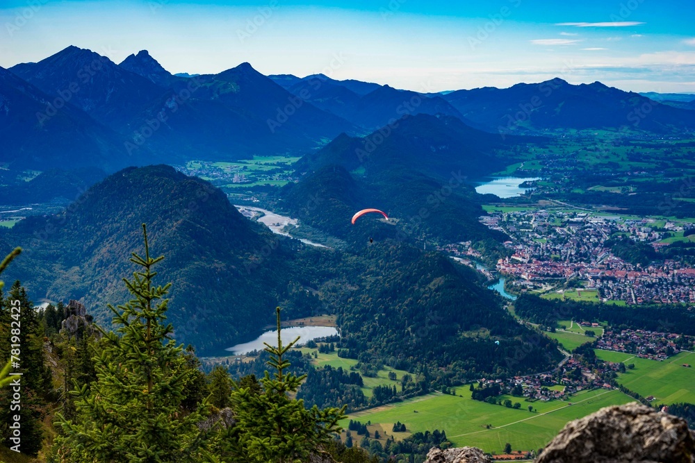 Paraglider flying over greenery mountain landscape with dense trees and buildings