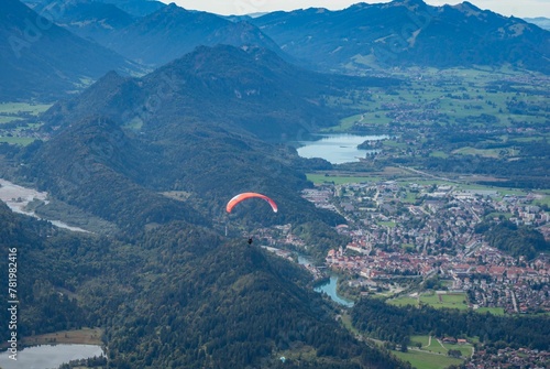 Paraglider flying over greenery mountain landscape with dense trees and buildings