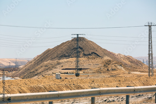 Large mound of earth near power lines under a clear sky in a desert environment. A vast mounds against the backdrop of a desert landscape, with electric power lines crossing in the foreground, Israel