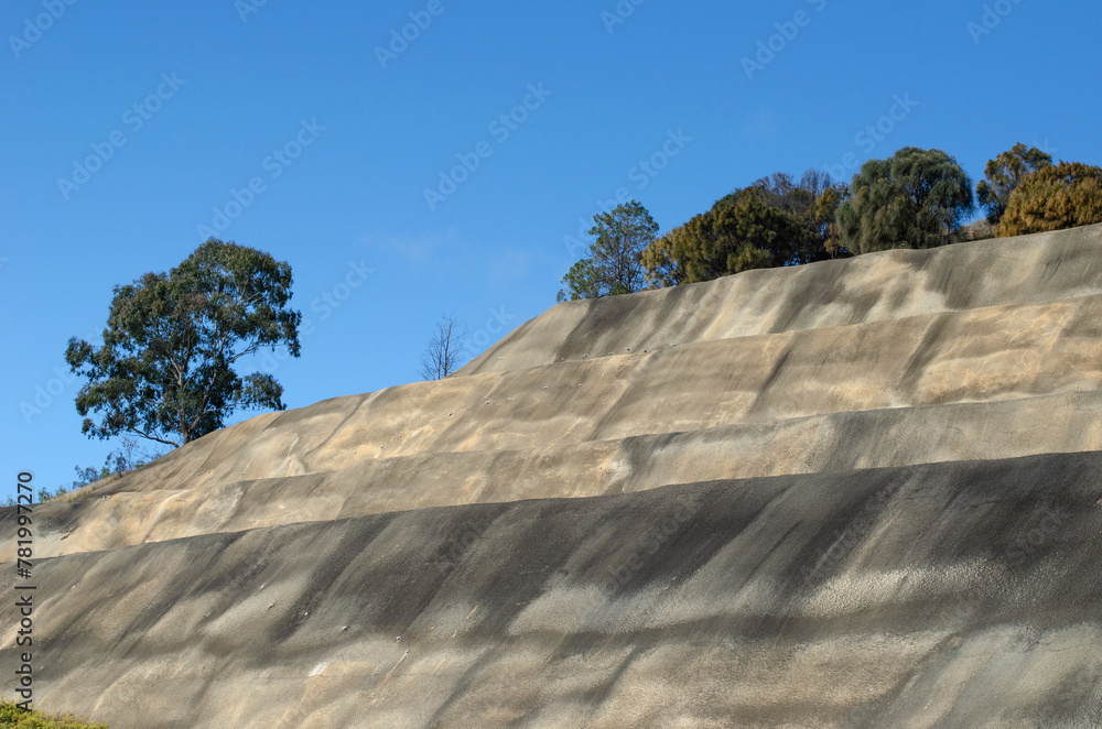 A tall concrete retaining wall or mechanically stabilized earth MSE wall, used alongside highways and in steep terrain to prevent soil erosion and landslides. A tall concrete retaining wall or mechanically stabilized earth MSE wall, used alongside highways and in steep terrain to prevent soil erosion and landslides.