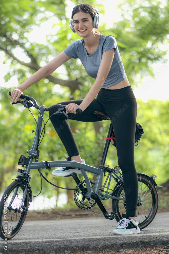 Naklejka premium Happy young beautiful woman enjoy riding bicycle outdoor in public park. Young adult mixed-race woman has fun cycling outside to exercise and recreation in sunlight. Active person healthy lifestyle.