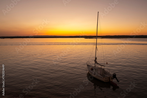 A pleasure sailboat anchored on a beach at sunset with orange sky on the horizon in the background © mestock