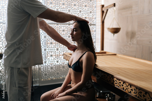 Professional masseur male doing massage head and shoulder for young woman in spa salon by window. Pretty female getting head massage by masseur in wellness center. Concept of rest with spa treatment.