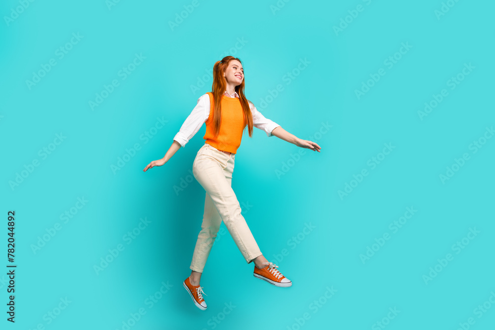 Photo of optimistic positive cute girl wear orange trendy clothes fly air walk empty space isolated on aquamarine color background