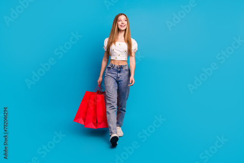 Full length portrait of lovely girl hold bags walk look empty space wear top isolated on blue color background