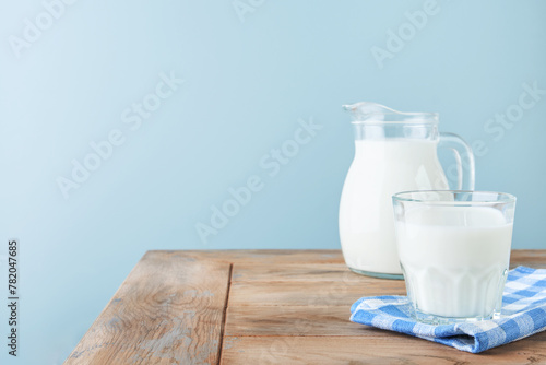 Milk in jug and glass on wooden table and blue background. Concept of farm dairy products, milk day. Kitchen or supermarket mock up for design. Copy space.