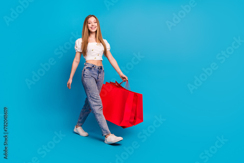 Full length portrait of lovely girl shop bags walk empty space wear top isolated on blue color background
