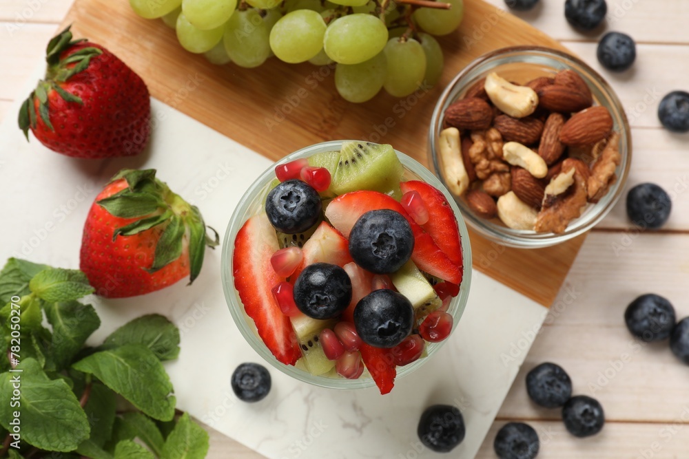 Healthy breakfast. Delicious fruit salad in glass, nuts and ingredients on light wooden table, flat lay Healthy breakfast. Delicious fruit salad in glass, nuts and ingredients on light wooden table, flat lay