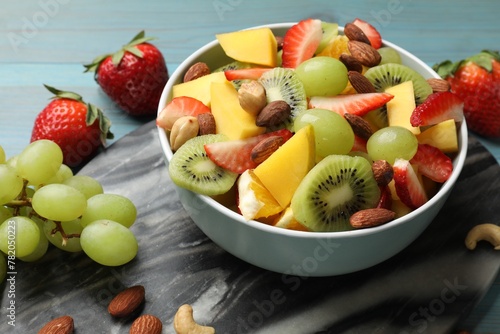 Tasty fruit salad in bowl and ingredients on table, closeup