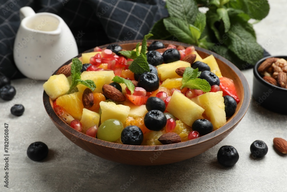 Delicious fruit salad in bowl, berries, nuts and fresh mint on grey table Delicious fruit salad in bowl, berries, nuts and fresh mint on grey table