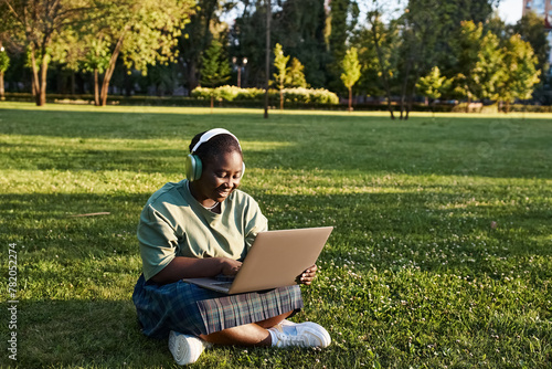 Plus size African American woman enjoying nature while working on a laptop computer in the grass on a sunny day. © LIGHTFIELD STUDIOS