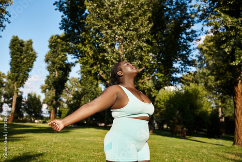 Billede på lærred A curvy African American woman in a blue dress standing elegantly in a lush green grass field